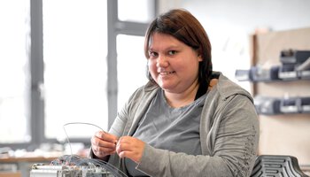 Eine junge Mitarbeiterin arbeitet mit Kabeln und lächelt | © Wendelstein Werkstätten