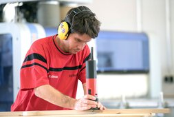 Ein Mitarbeiter mit Ohrenschutz bearbeitet Holz | © Wendelstein Werkstätten